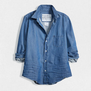 A Barry Tailored Button-Up in Famous Denim Vintage Stonewashed Indigo from Frank & Eileen, featuring rolled-up sleeves, set against a white textured background. Crafted from Italian Denim, this shirt showcases a single chest pocket and an inner collar label that reads "Frank & Eileen EST 1947." The fabric has a softly worn, slightly wrinkled appearance.