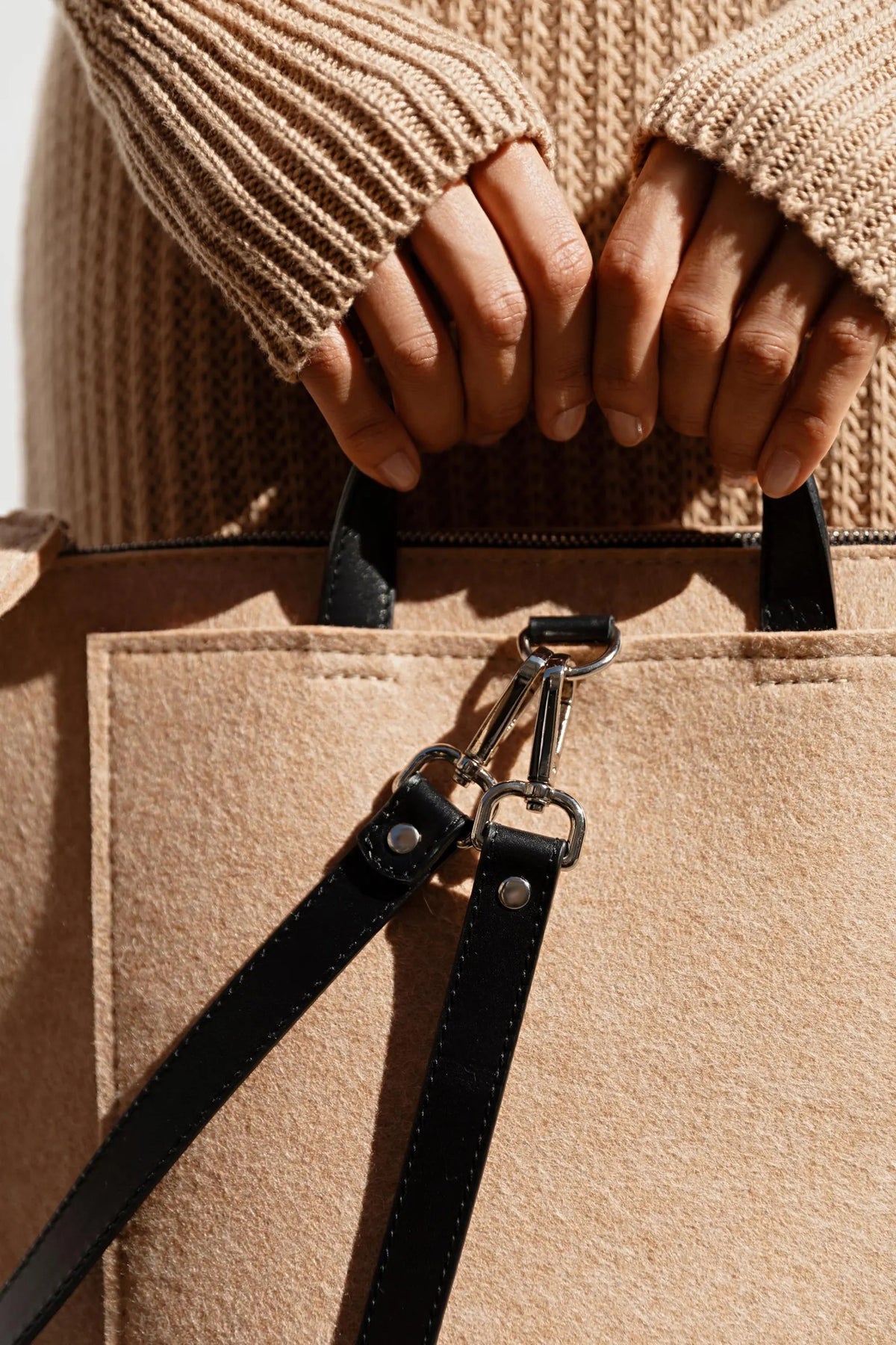 A person in a beige trench coat holds the WOOLBERRY WOOL FELT LONG TOTE BAG with black handles, standing against a plain, light-colored background.