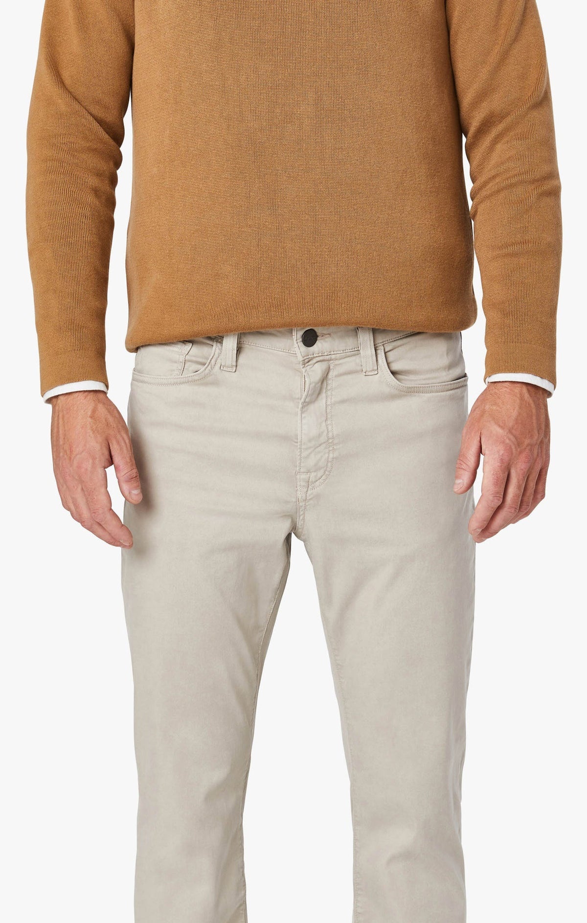 A bearded man stands against a plain background, wearing a tan blazer, a brown sweater over a white shirt, and 34 HERITAGE - CHARISMA RELAXED STRAIGHT LEG PANT IN DAWN TWILL. He adjusts his blazer sleeve with one hand.