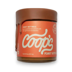 A 10 oz (283.5 g) jar of COOPS Peanut Butter Sauce, handmade in small batches to perfection, features chocolate-like drips down the lid and an orange label with “Sweet Nuttiness” and “Peanut Butter Sauce.”.