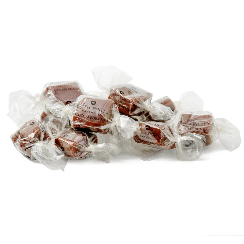 A clear bag of MOUTH PARTY - CHOCOLATE SEA SALT caramels from MOUTH PARTY, tied with a shiny brown ribbon. The label features a pink lips logo and product details.