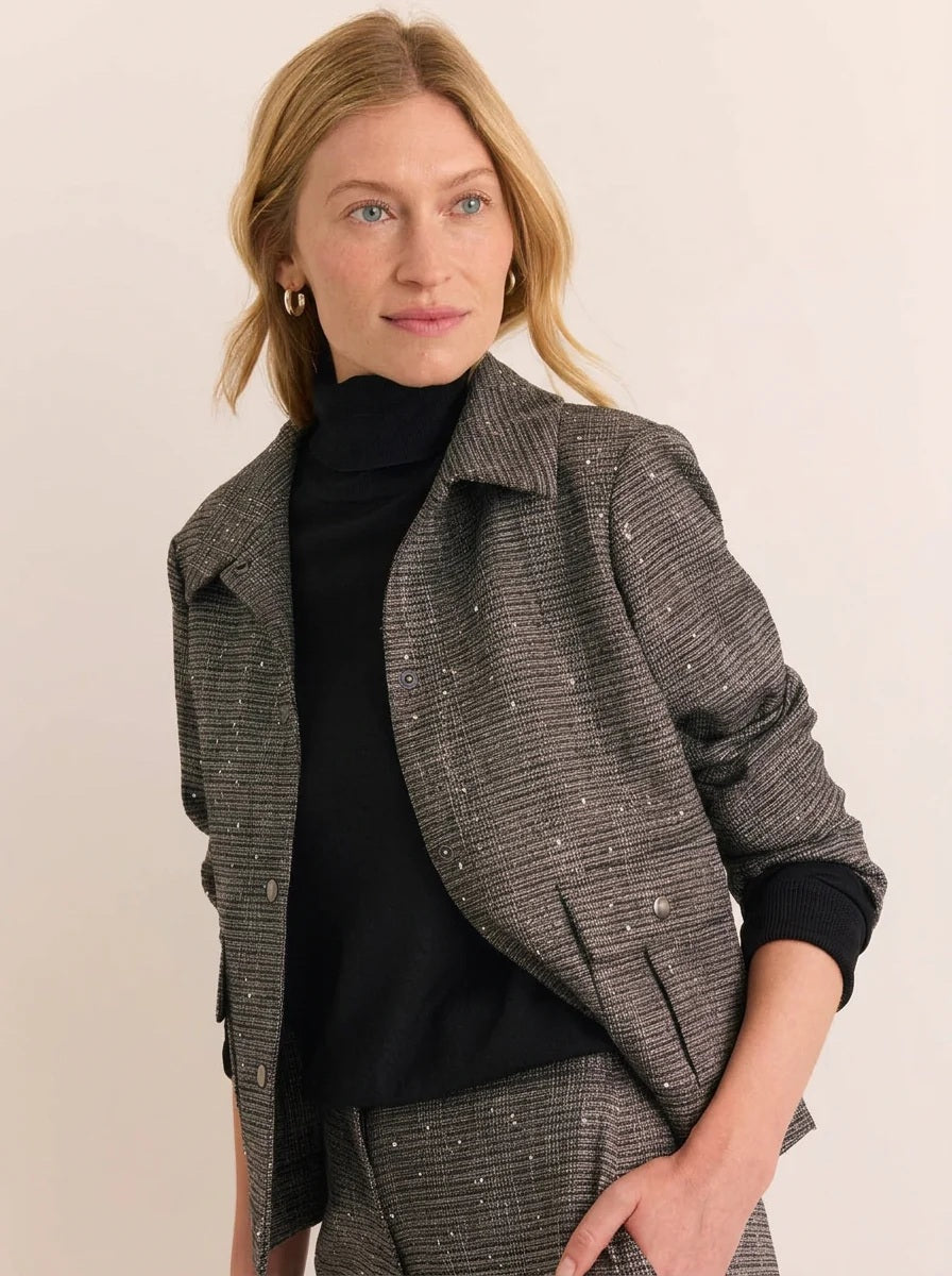 A woman wears a charcoal gray HINSON WU - HANNAH LONG SLEEVE TWEED JACKET WITH SEQUINS, a black turtleneck, and matching tweed trousers, holding a black clutch.