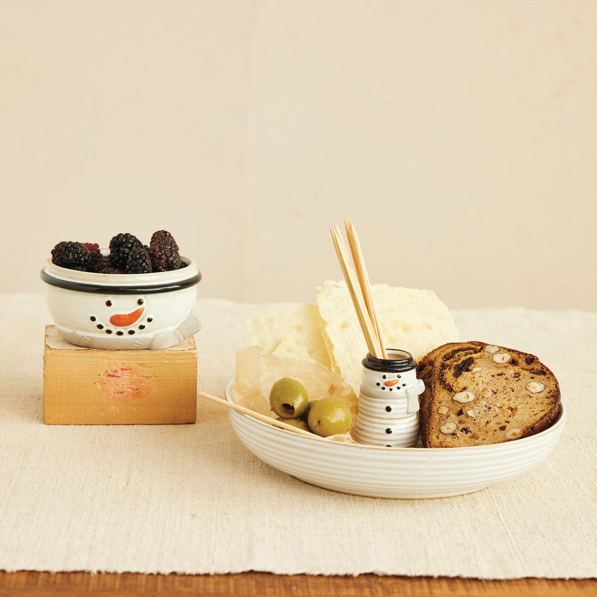 The CREATIVE COOP STONEWARE BOWL WITH SNOWMAN SHAPED TOOTHPICK HOLDER features a circular, ribbed design with a central opening and a glossy white finish, shown in top and side views.