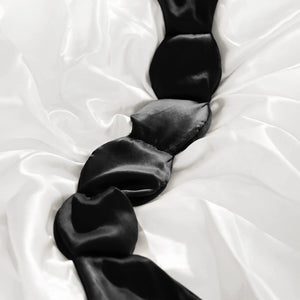 The NODPOD Silk Weighted Sleep Eye Mask in Noir by NODPOD is a dark blue, segmented eye mask featuring a strap-free design and unique four-pad shape. Text highlights its calming effect for stress relief and relaxation, all set against a light background.