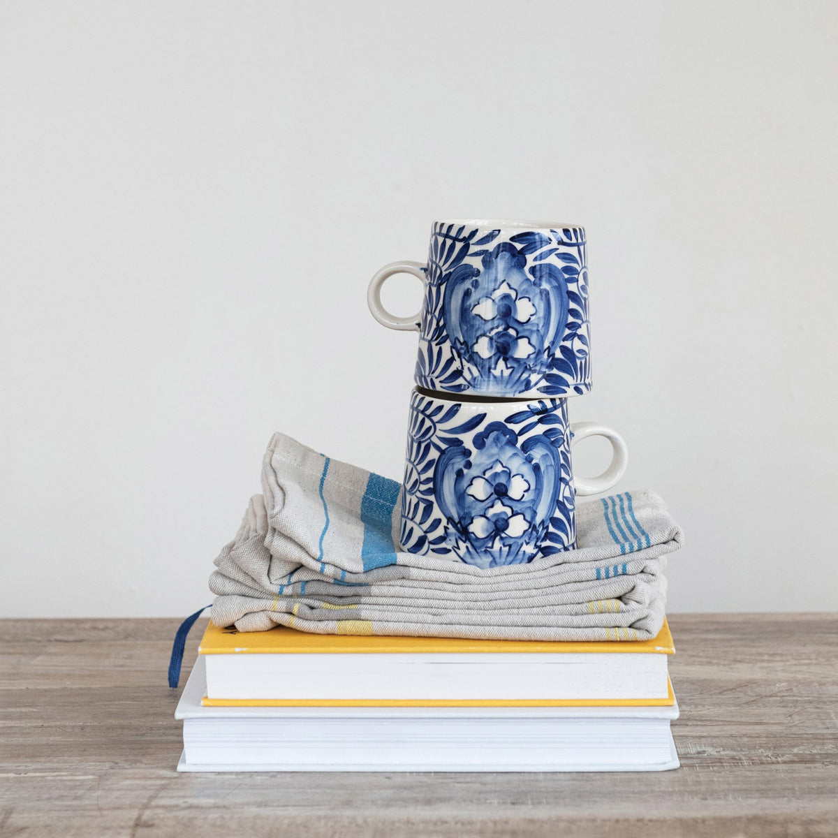 The CREATIVE COOP CREAM AND BLUE HAND-PAINTED STONEWARE MUG features a blue floral and leaf design on white, a handle, tapered shape, and glossy finish—bringing artisanal charm to your daily coffee.