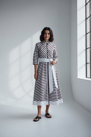 A blurry image shows the MILVA MI Cotton Poplin Dress by MILVA, featuring biscotto tan and white stripes in three horizontal bands—white at the top and bottom, and a wide tan band in the center.