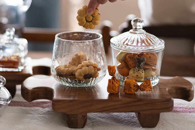 Two ETUHOME Bistro Glass Bon Bon Jars with ribbed lids sit on a wooden surface, one filled with yellow candies and the other nearly empty. Wrapped sweets are scattered nearby, creating a charming ETUHOME display.