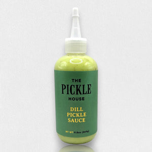 A 9.5-oz squeeze bottle of THE PICKLE HOUSE brand DILL PICKLE SAUCE, with a green label and white cap, sits on a light gray textured background. This Dill Garlic sauce is perfect as a marinade or salad dressing.