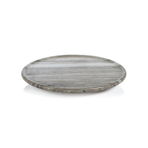 The ZODAX CREMA MARFIL MARBLE LAZY SUSAN, a round 16-inch grey and white serving platter, sits on a textured grey surface with a gold-colored metal spatula resting at its edge.