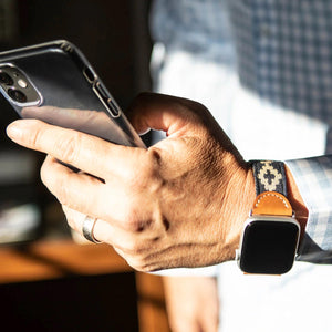 The LA MATERA - CORBINA Apple Watch Band in silver pairs artisan brown leather with a black fabric section, beige geometric pattern, and red stitching.