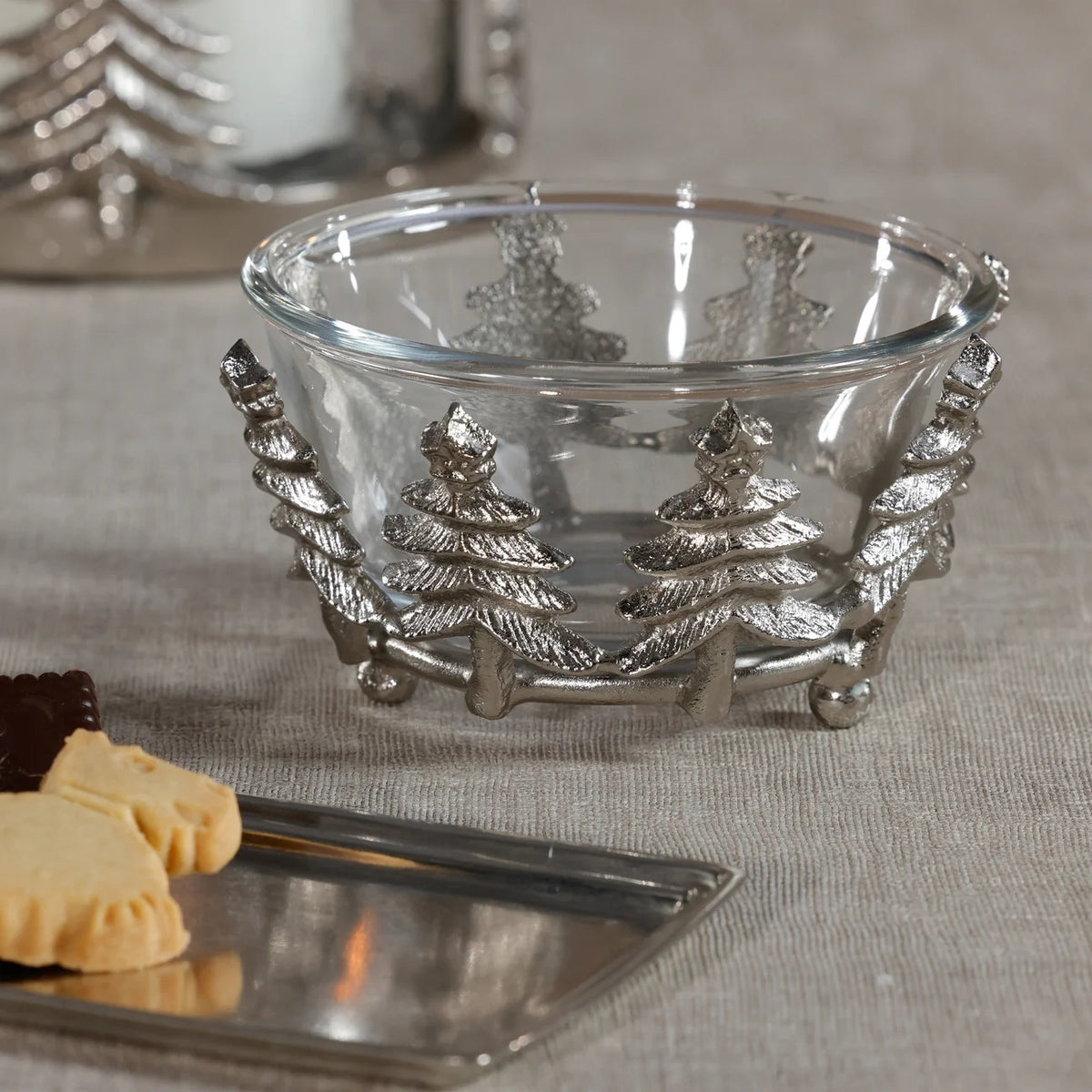 ZODAX GLASS AND ALLOR BOWL: a 5.5 in x 3 in clear glass bowl set in a silver-toned aluminum base featuring a decorative row of evergreen trees.