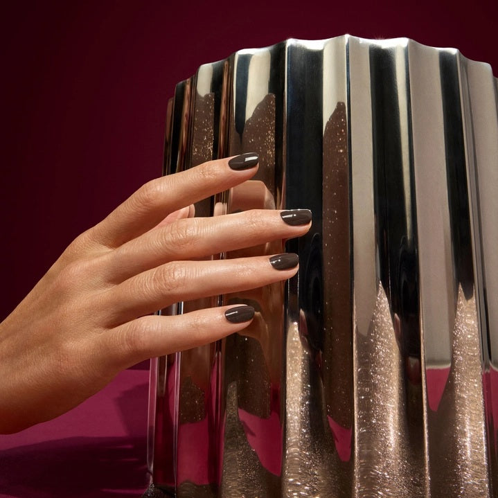 A bottle of MANUCURIST INC GREEN™ Nail Polish in the shade MOCHA, featuring a dark brown color, a black cap, and a white label that reads “QUICK DRY INTENSE COLOR.”.