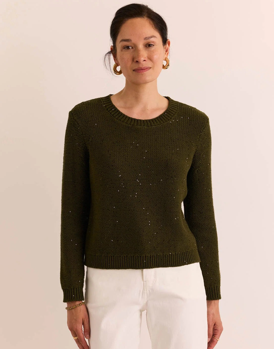 A person wearing the HINSON WU Queenie Long Sleeve Sequin Sweater in Oregano—an everyday essential crafted from breathable cotton with subtle sequin embellishments—paired with gold hoop earrings and touching their collar with one hand.