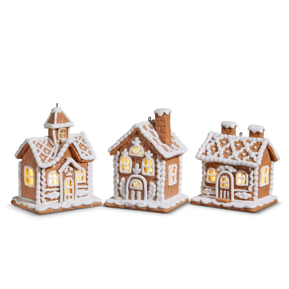 Three RAZ IMPORTS LIGHTED GINGERBREAD HOUSE ORNAMENTS, crafted from clay dough with white icing accents and glowing yellow lights inside, are displayed side by side against a white background.