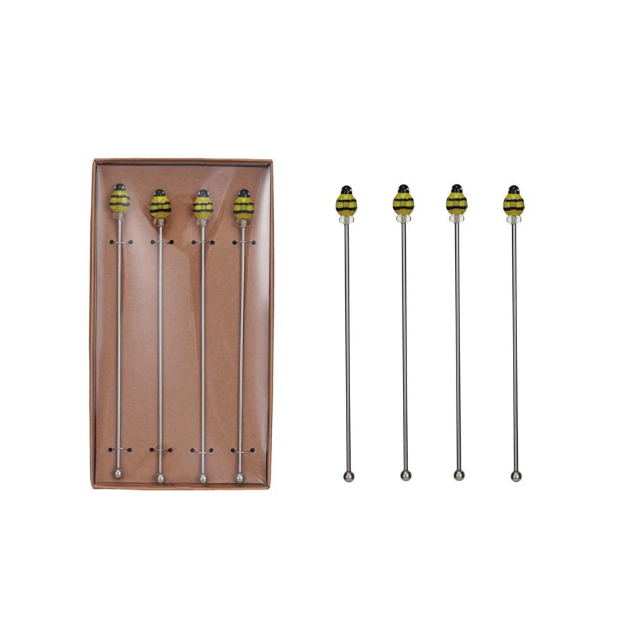 Five CREATIVE COOP STAINLESS STEEL BEE COCKTAIL STIRRERS are displayed, four neatly arranged in a brown box with dotted placeholders and one positioned outside the box. To the right, three identical stirrers are laid out side by side on a white background, showcasing their versatile utility.