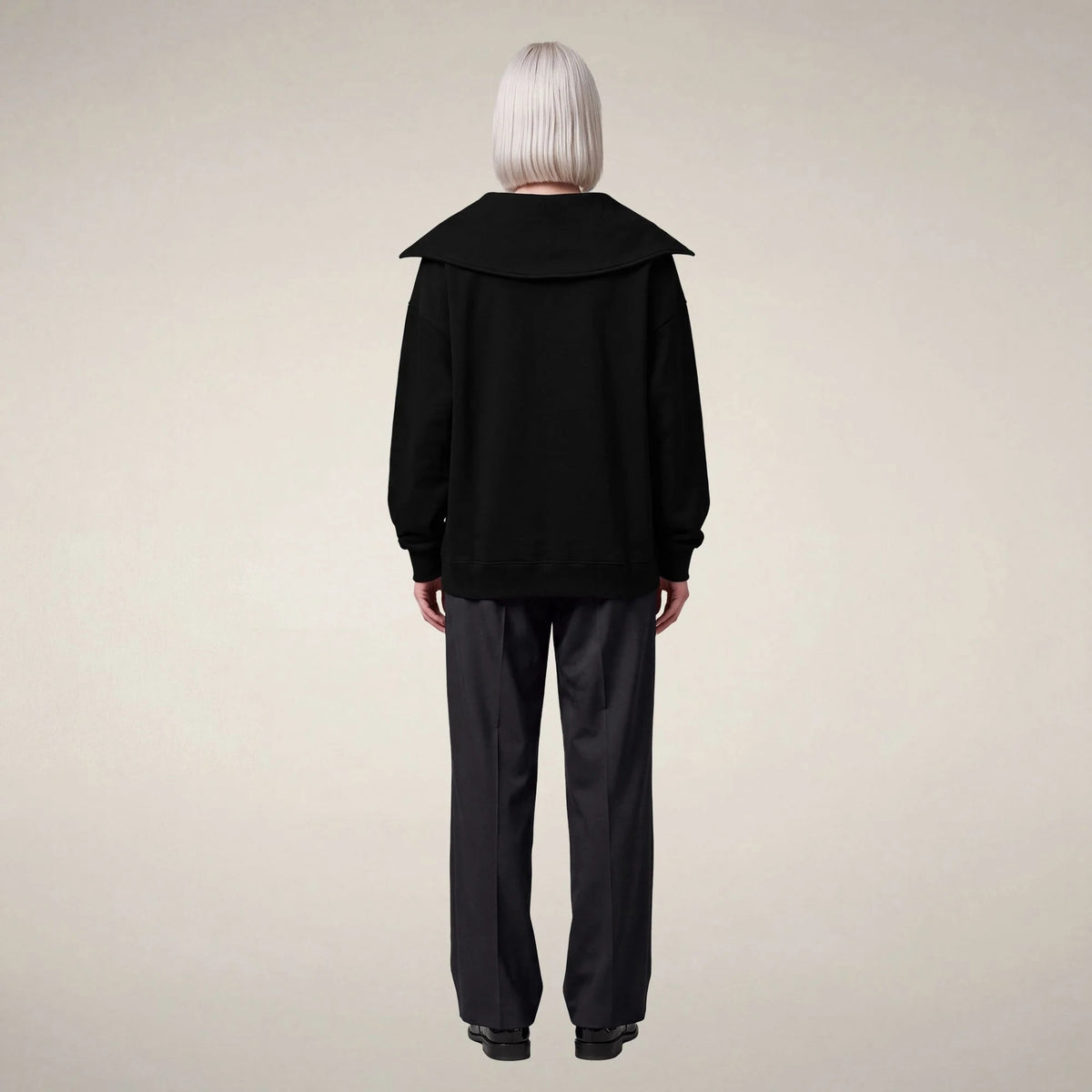A person seen from behind, wearing a sleek, modern black SAVE THE DUCK - HINATA HALF ZIP TOP with a large collar and dark trousers.