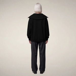 A person seen from behind, wearing a sleek, modern black SAVE THE DUCK - HINATA HALF ZIP TOP with a large collar and dark trousers.