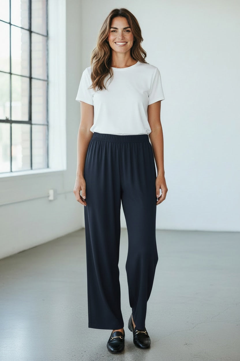 A person wearing MEIMEIJ PULL ON STRAIGHT LEG LONG PANTS in black and a red top, shown from the waist down, stands against a light textured background.