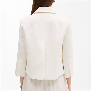 A person is wearing the MEIMEIJ - WHITE SHORT JACKET WITH SCALLOPED POCKETS, paired with a matching white top. The jacket, from the brand MEIMEIJ, features a notched collar and three-quarter sleeves. Complementing the outfit, they accessorize with a delicate necklace and a bracelet on their right wrist.