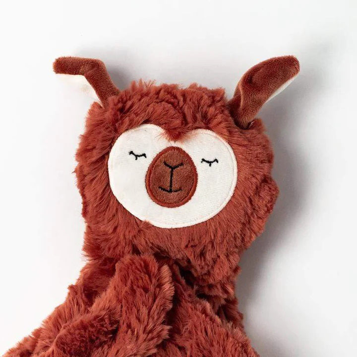 A cuddly SLUMBERKINS Alpaca Snuggler in rust is nestled in a white box adorned with the SLUMBERKINS logo. It includes a book titled "Alpaca," aimed at enhancing early emotional learning and managing anxiety.