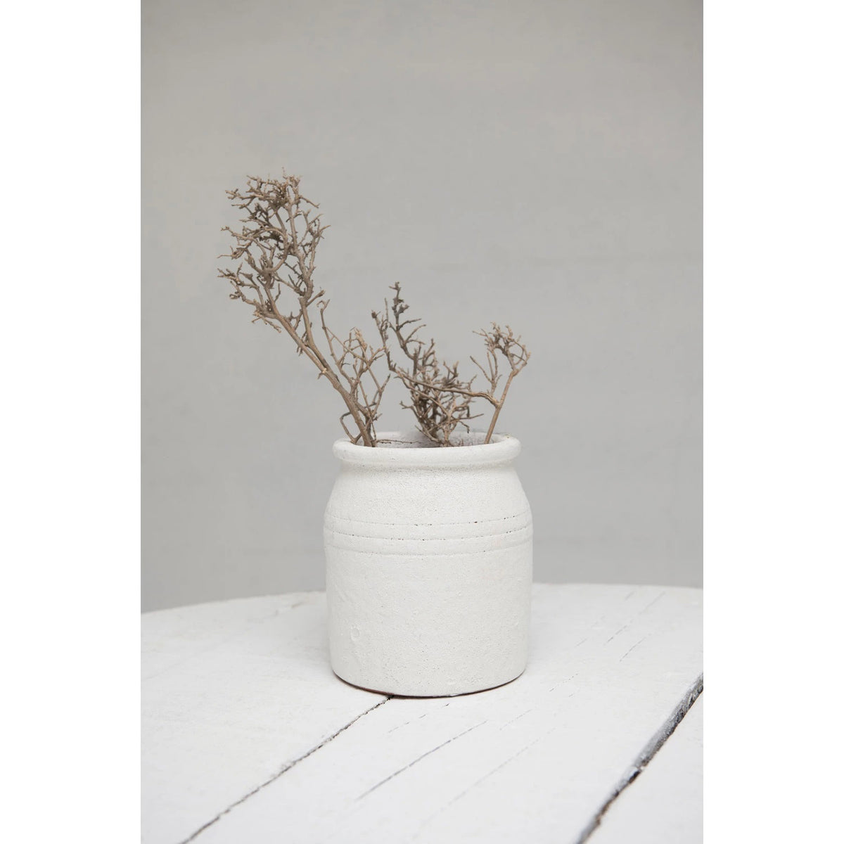 The DISTRESSED TERRACOTTA CROCK by CREATIVE COOP is a rustic, off-white earthenware pot with a cylindrical shape and slightly flared rim, featuring a textured finish. This charming piece adds timeless elegance to any home décor.