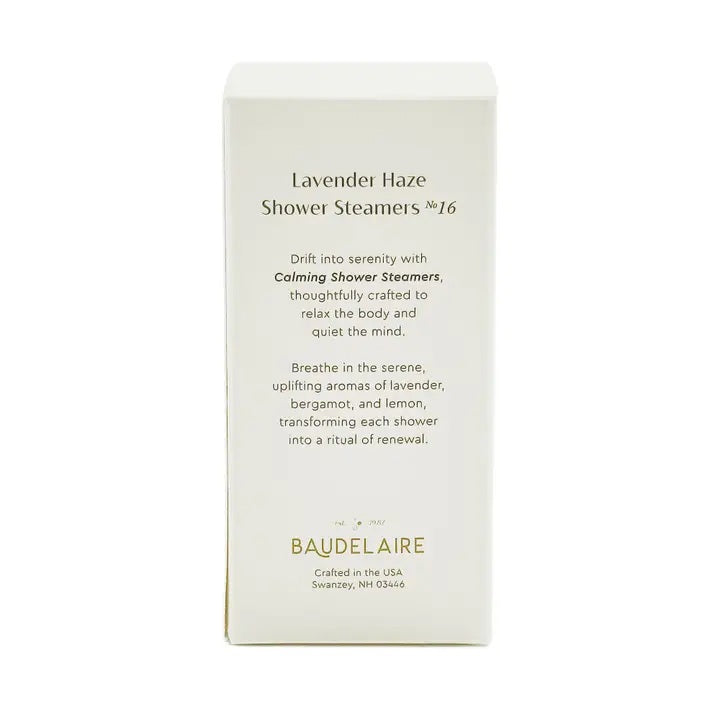 A BAUDELAIRE - CALM LAVENDER HAZE SHOWER STEAMER rests atop a slatted bamboo soap dish emblazoned with “BAUDELAIRE,” water droplets scattered on the white surface below—creating a tranquil scene evocative of soothing aromatherapy.