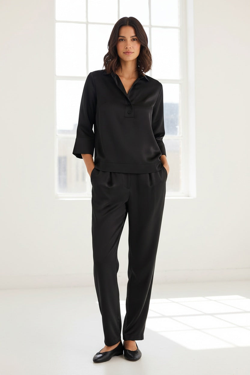 A woman with blonde hair models the HINSON WU Aileen 3/4 Sleeve Liquid Satin Shirt in black, featuring a collar and button details, against a plain light background.