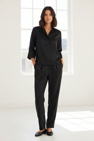 A woman with blonde hair models the HINSON WU Aileen 3/4 Sleeve Liquid Satin Shirt in black, featuring a collar and button details, against a plain light background.