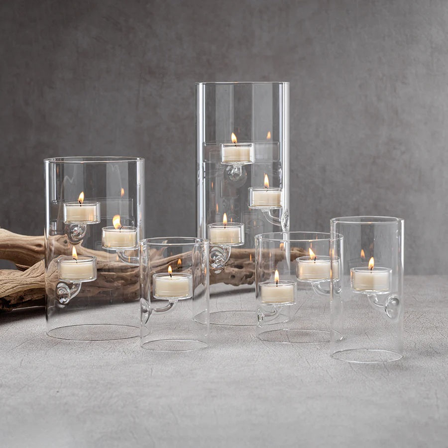 A SUSPENDED GLASS TEALIGHT HOLDER - LARGE by ZODAX holds several red-lit tealights, accented with pine branches and berries on a white surface, all set against a vibrant red background.
