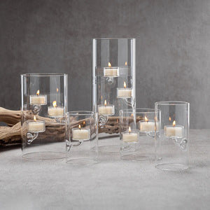 A SUSPENDED GLASS TEALIGHT HOLDER - LARGE by ZODAX holds several red-lit tealights, accented with pine branches and berries on a white surface, all set against a vibrant red background.