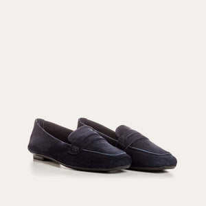 Six pairs of REQINS HEMA suede loafers in marine, featuring a classic penny loafer design and timeless silhouette, are displayed on a light tan surface in various blue and green shades.