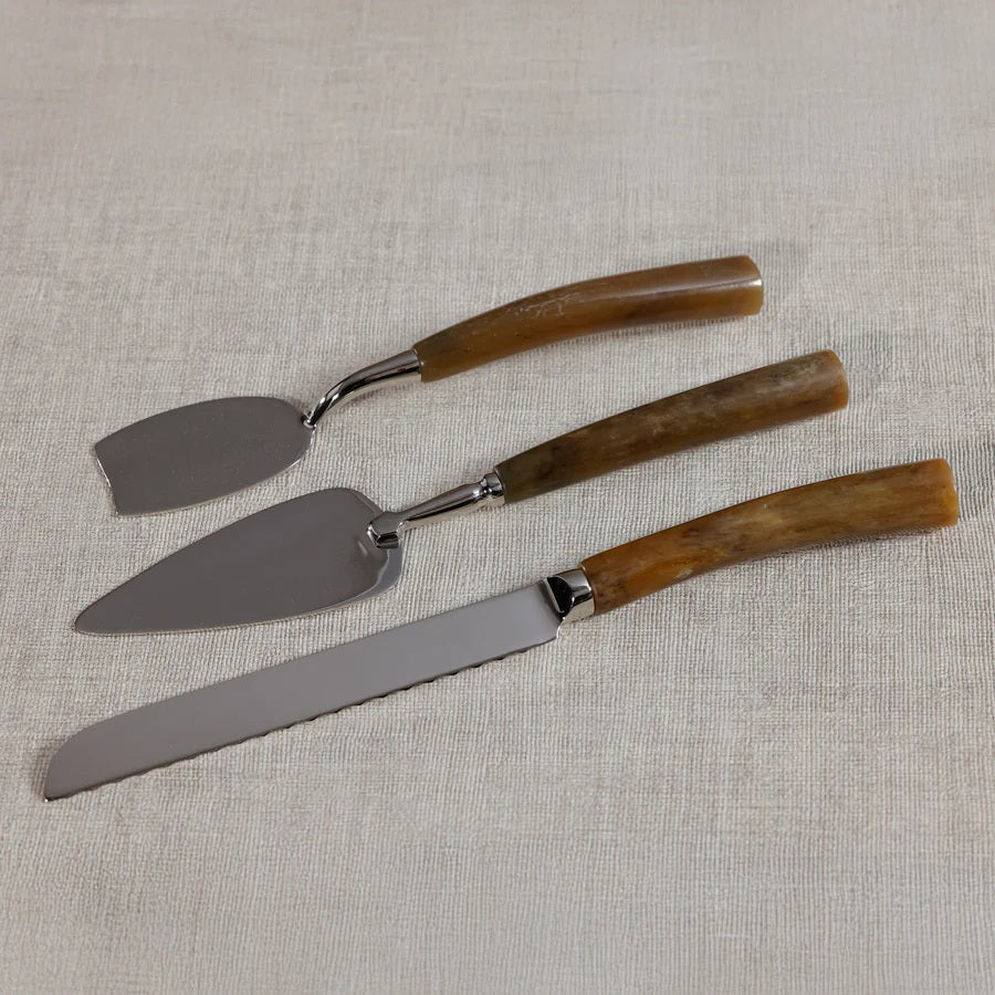 Three stainless steel utensils from the ZODAX GOURMET CHEESE KNIFE SET—a cake server, a serrated cake knife, and a pie server—feature brown curved handles and are arranged side by side on a white background. Perfect for an elegant cheese board presentation, these versatile tools showcase sleek design and impeccable craftsmanship, making them the ideal complement to any gourmet setting.