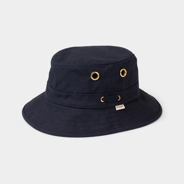 A young person with fair skin and light brown hair wears the TILLEY - ICONIC T1 BUCKET HAT IN DARK NAVY and a light gray crew-neck shirt, looking directly at the camera against a plain, light background.