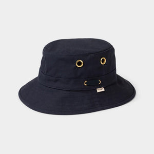 A young person with fair skin and light brown hair wears the TILLEY - ICONIC T1 BUCKET HAT IN DARK NAVY and a light gray crew-neck shirt, looking directly at the camera against a plain, light background.