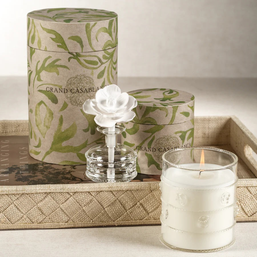 A set of MINI GRANDCASABLANCA PORCELAIN DIFFUSER - 1.7 OZ by ZODAX sit on marble; two display ceramic flower toppers, while others glow softly, filling the air with subtle wild tuberose notes.