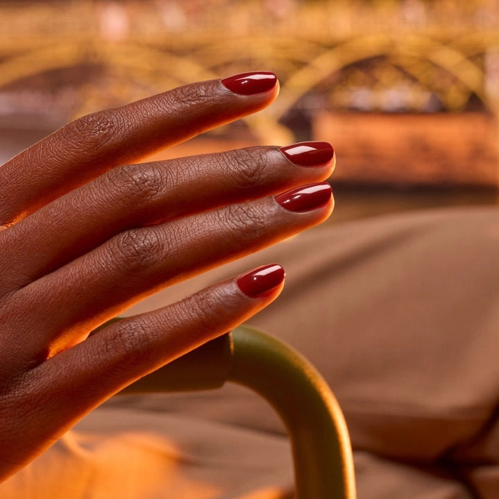 A close-up of MANUCURIST - GREEN™ NAIL POLISH IN BOHEMIAN by MANUCURIST INC being smoothly applied with a brush, revealing its glossy, reflective red finish and visible bristle strokes.