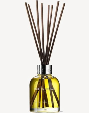 The MOLTON BROWN Coastal Cypress Diffuser 150ml features a glass bottle with yellow liquid, silver cap, and dark brown reeds, releasing an aromatic scent inspired by a gentle sea breeze.
