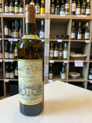 A bottle of CHATEAU SIMONE PALETTE BLANC 2021 by WINE: HAW RIVER WINE MAN features a detailed illustrated label with a chateau, vineyards, gold accents, brown foil capsule, and vintage year near the neck, evoking its historic Provencal estate origins.