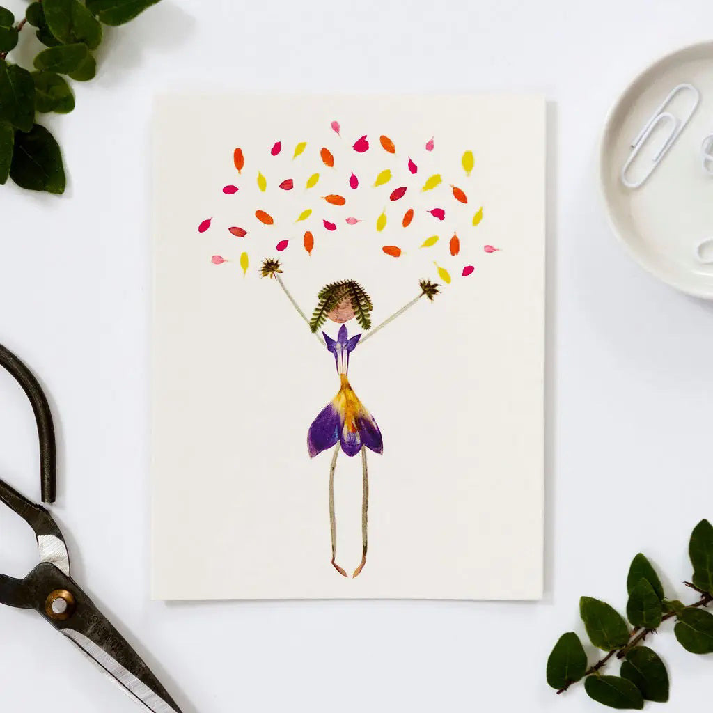 The PETAL PEOPLE PRESS - CONFETTI CARD by PETAL PEOPLE PRESS is a blank greeting card featuring a whimsical figure in a purple and yellow dress with green hair, arms raised, surrounded by colorful confetti. Envelope included.