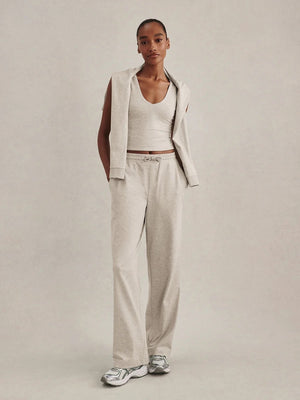 A woman wearing a light gray Varley Motion Easy Jogger 30 in Pebble Marl tank top and matching wide-leg joggers with athletic shoes.