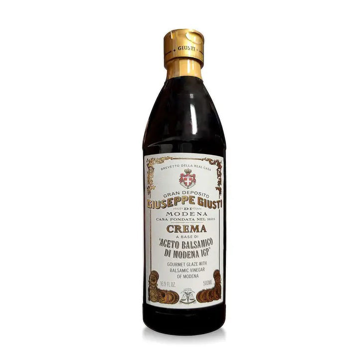 A bottle of GIUSEPPE GIUSTI - CREAM CLASSIC BALSAMIC GLAZE from MERCATO DI BELLINA features a gold cap and a label adorned with intricate designs and Italian text, highlighting its premium quality. The dark-colored glaze inside the clear bottle is visible, ideal for creating a delectable balsamic reduction.