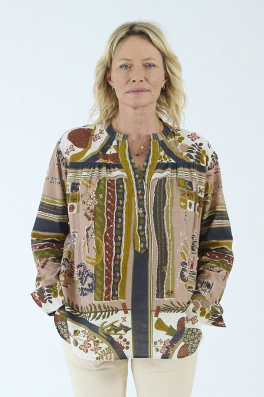 A person with blonde, shoulder-length hair is shown from the back against a plain light background, wearing the STORIATIPIC - MARGOT BLOUSE IN DELYS by STORIATIPIC—a colorful, patterned long-sleeve blouse crafted from 100% cotton for comfort and breathability. This top pairs effortlessly with light pants and is ideal for gentle machine wash and easy cotton care.
