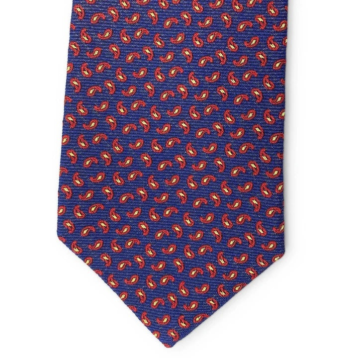 A rolled-up Camden Silk Tie in navy by Bird Dog Bay, featuring a red and yellow paisley pattern and complete with a Peter-Blair woven label, displayed on a white background.