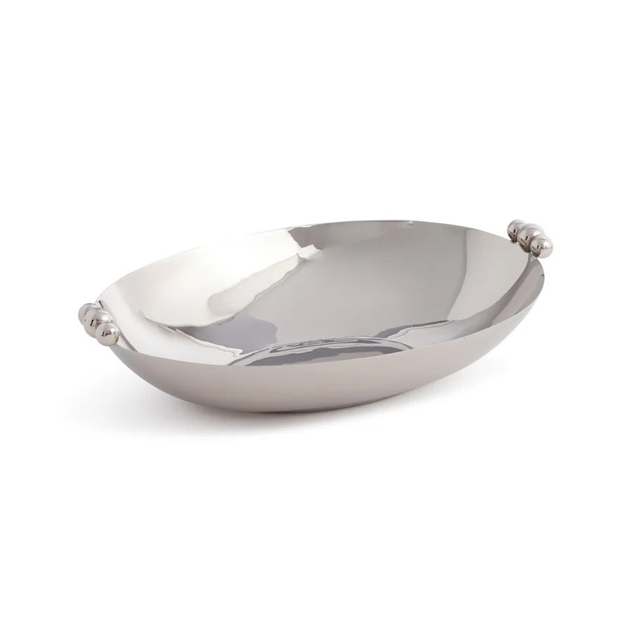 The ZODAX POLISHED NICKEL SERVING BOWL, featuring small rounded handles on each end, is displayed on a glittery surface with sparkling cubic decorations in the background.