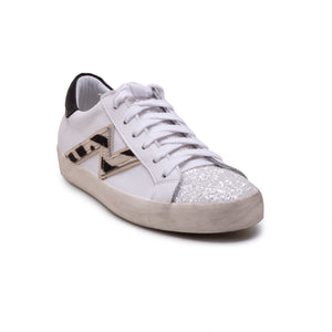 The MICHELE LOPRIORE - NINA SNEAKER is crafted from soft leather and features white laces, a silver glitter-covered toe cap, and a beige and black zigzag design on the side. It includes an extra light rubber sole with a height of 2.5 cm, a slightly worn midsole, and a black heel tab. Displayed against a plain white background, this stylish sneaker seamlessly blends elegance with contemporary flair.