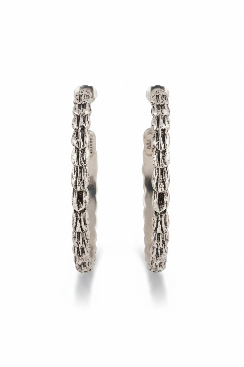 Introducing the GAS BIJOUX - LIANE SILVER HOOP EARRINGS: a stunning pair of 4.5 cm diameter, silver-plated earrings showcasing a twisted rope design set against a light background. These elegant hoops reflect subtle sophistication beneath them.