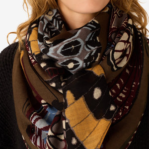 The INOUI EDITIONS - PAPILLONS WOOL SCARF IN KHAKI by INOUI is a square scarf made in India, featuring an intricate and colorful butterfly pattern in brown, blue, yellow, and white hues on a tan background. Measuring 130 x 130 cm, it provides generous coverage and stylish versatility for any occasion.