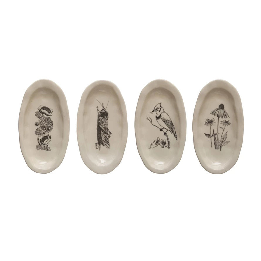The STONEWARE FLORA AND FAUNA CURIO DISH by CREATIVE COOP includes a set of four oval plates featuring black illustrations: a mushroom, grasshopper, bird on a branch, and flora with a coneflower, all arranged in a row against a plain background.