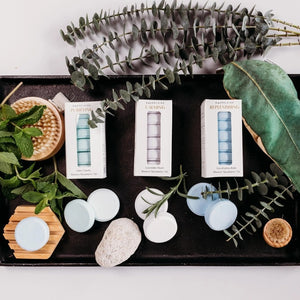 A white box labeled “BAUDELAIRE - REPLENISH EUCALYPTUS RAIN SHOWER STEAMER” by BAUDELAIRE, featuring a window that displays stacked round blue and white shower steamers inside, provides a refreshing aromatherapy experience with the invigorating scent of eucalyptus.