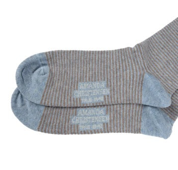 A pair of AMANDA CHRISTENSEN TRUE STRIPE MID-CALF SOCKS IN SKY BLUE MELANGE, featuring gray and brown stripes with light blue toes, heels, and cuffs. These Italian-made socks have printed text on the sole.